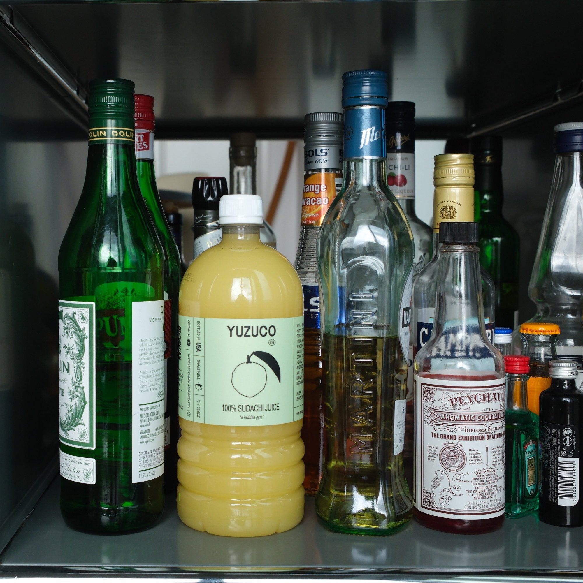100% Sudachi Juice Bottle in Liquor Cabinet next to other glass bottles.