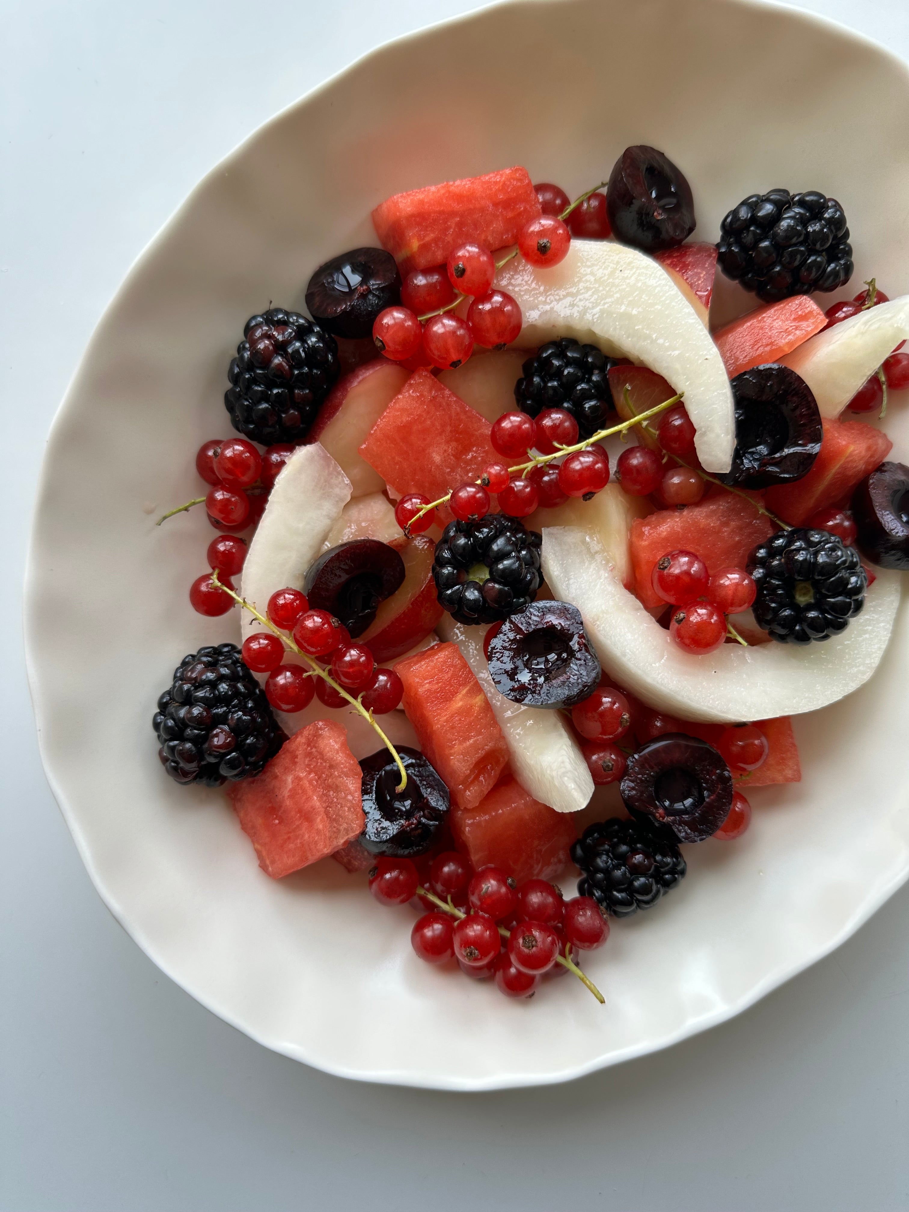 Top view of summer fruit plate with yuzu-honey glazed watermelon, melon, cherries, blackberries and red currants on a white plate