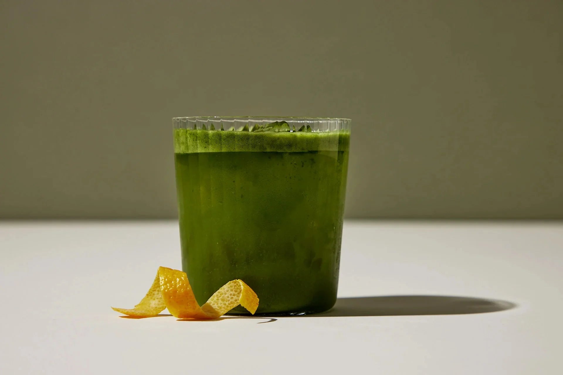 Close-up front view of iced yuzu matcha tonic showing frothy bright green drink with a curled yuzu peel on a white surface