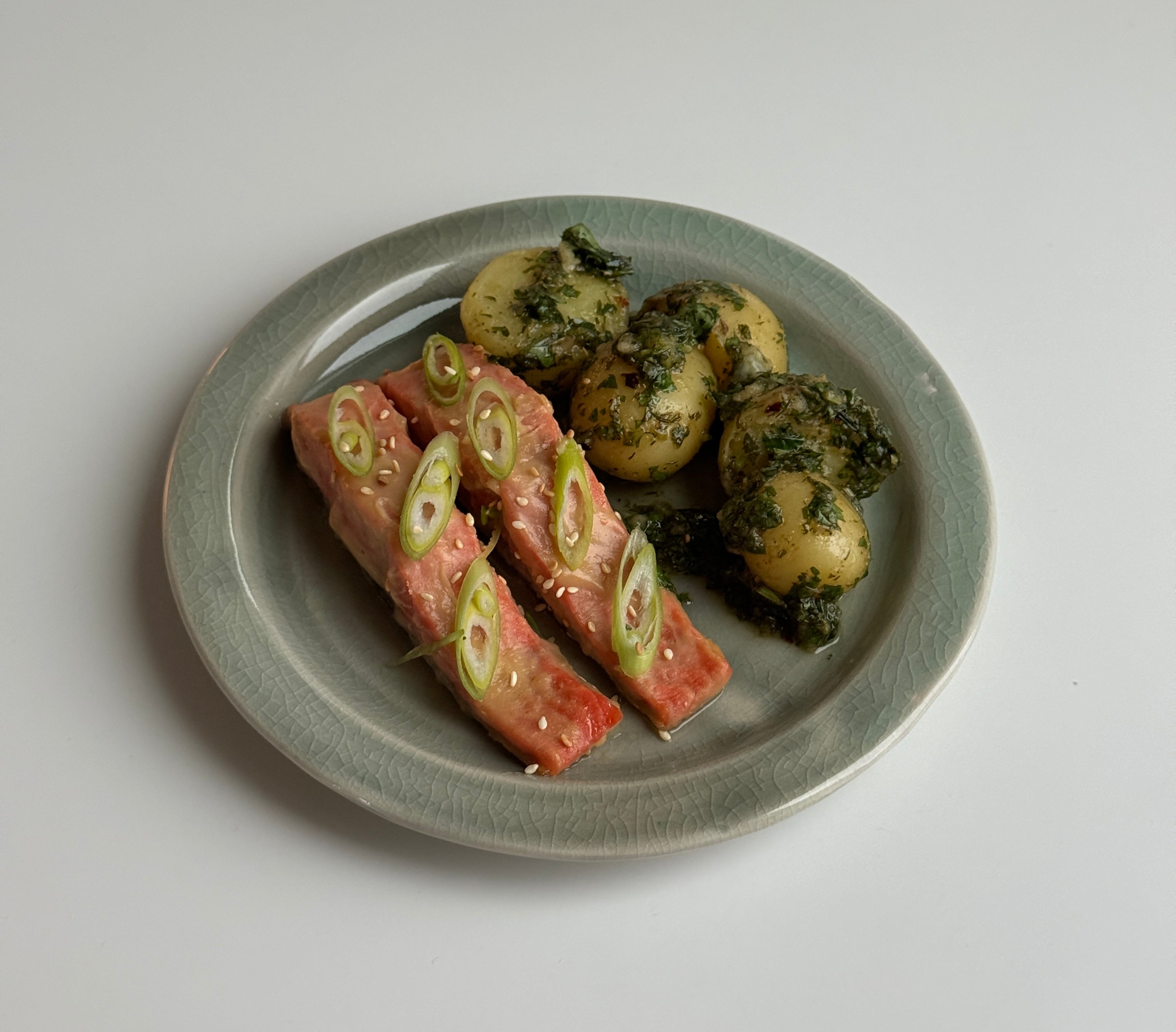 Herby yuzu potato salad with baby potatoes and seared salmon, garnished with sliced scallions on a gray ceramic plate against a white background