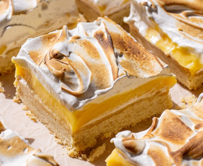 Close-up of yuzu meringue bar showing shortbread crust, bright yuzu curd, and toasted swirled meringue on parchment