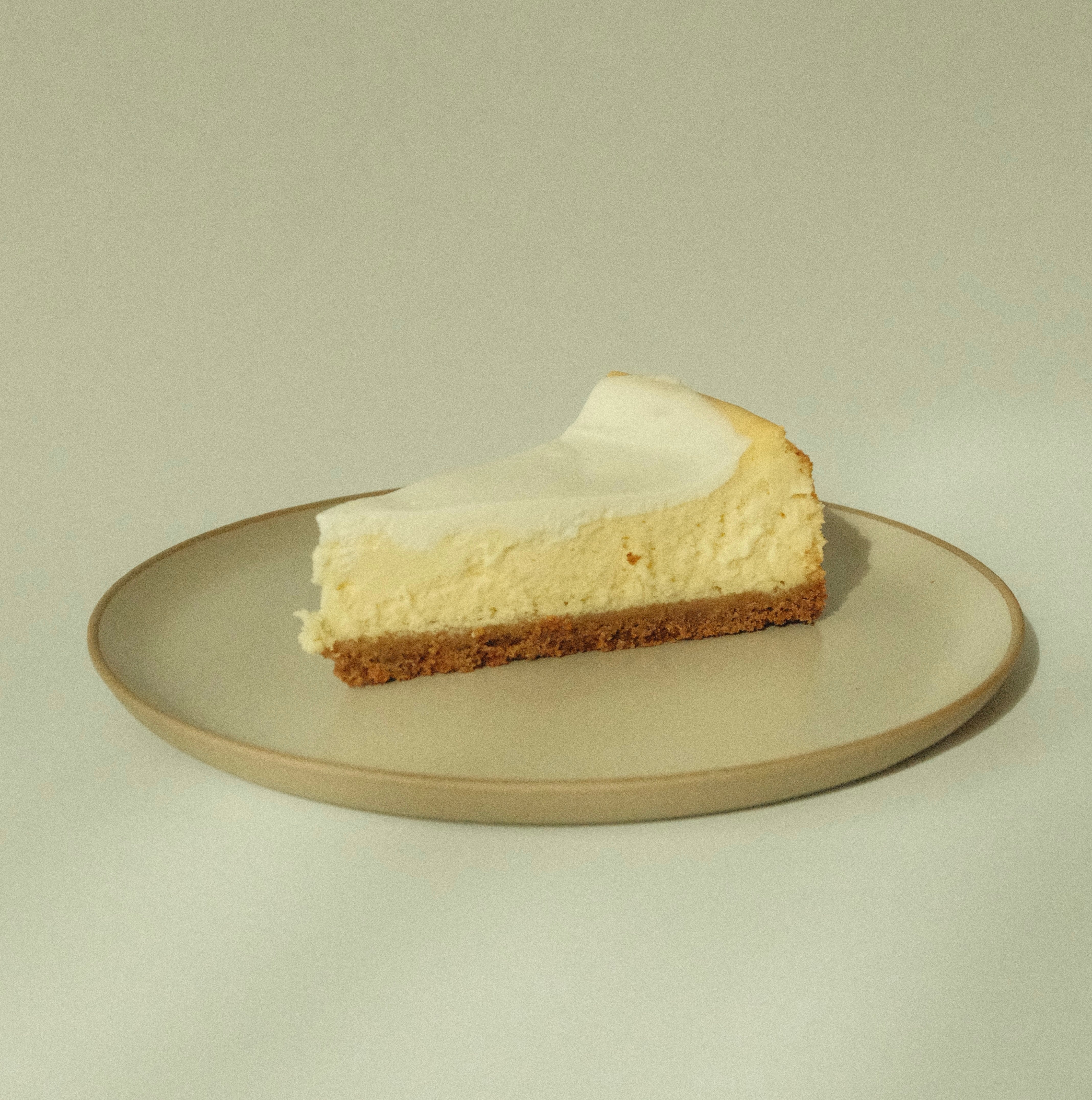 Side view of a slice of Sudachi cheesecake showcasing creamy filling, sour cream finish, and graham crust on a neutral beige plate