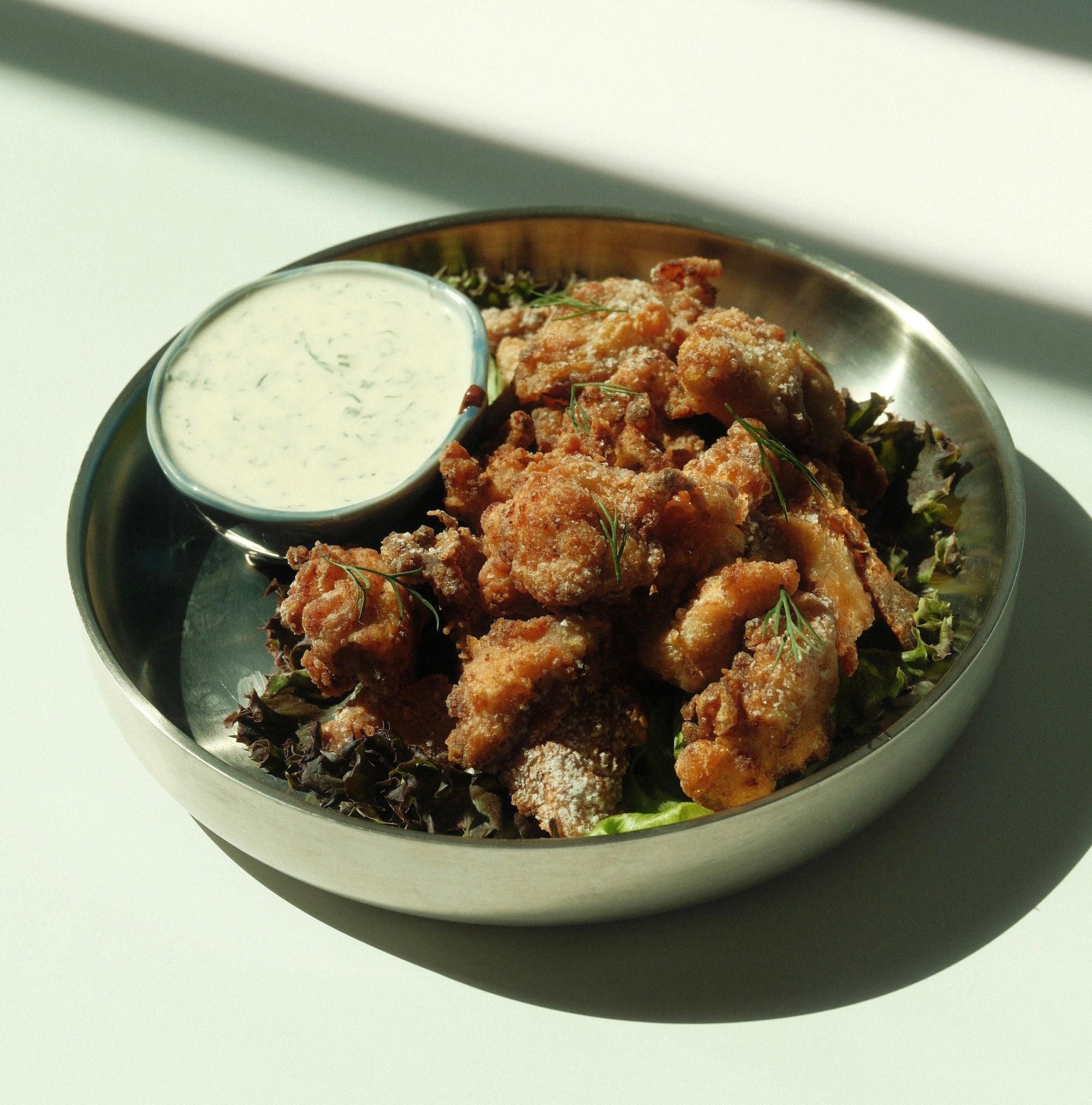 Yuzu-dusted karaage pieces served in a metal bowl on leafy greens with a small bowl of creamy yuzu ranch dipping sauce