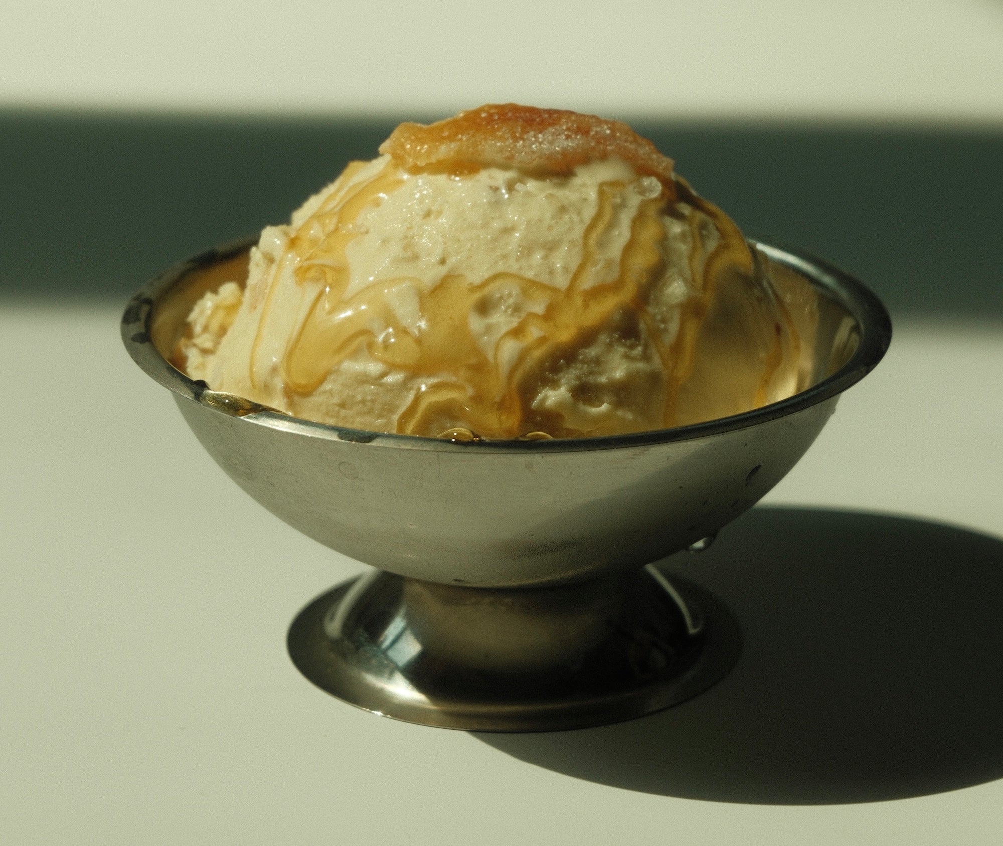 Close-up of yuzu honey ice cream in a metal dessert cup, topped with honey drizzle and a candied yuzu piece