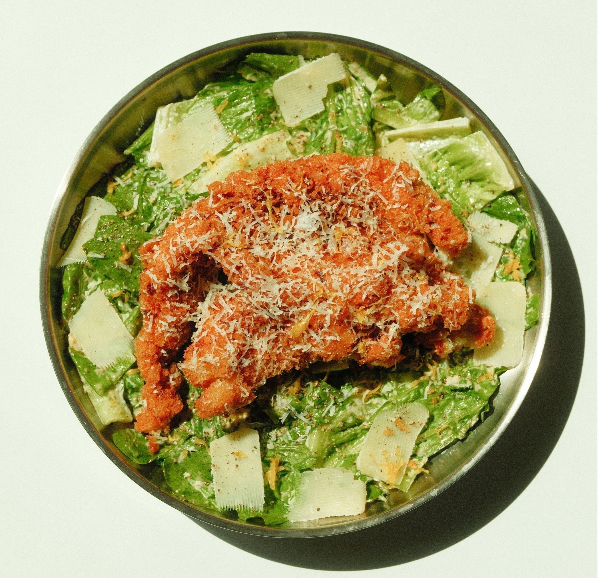 Overhead view of Yuzu Caesar salad with crispy breaded chicken and shaved Parmesan in a metal bowl
