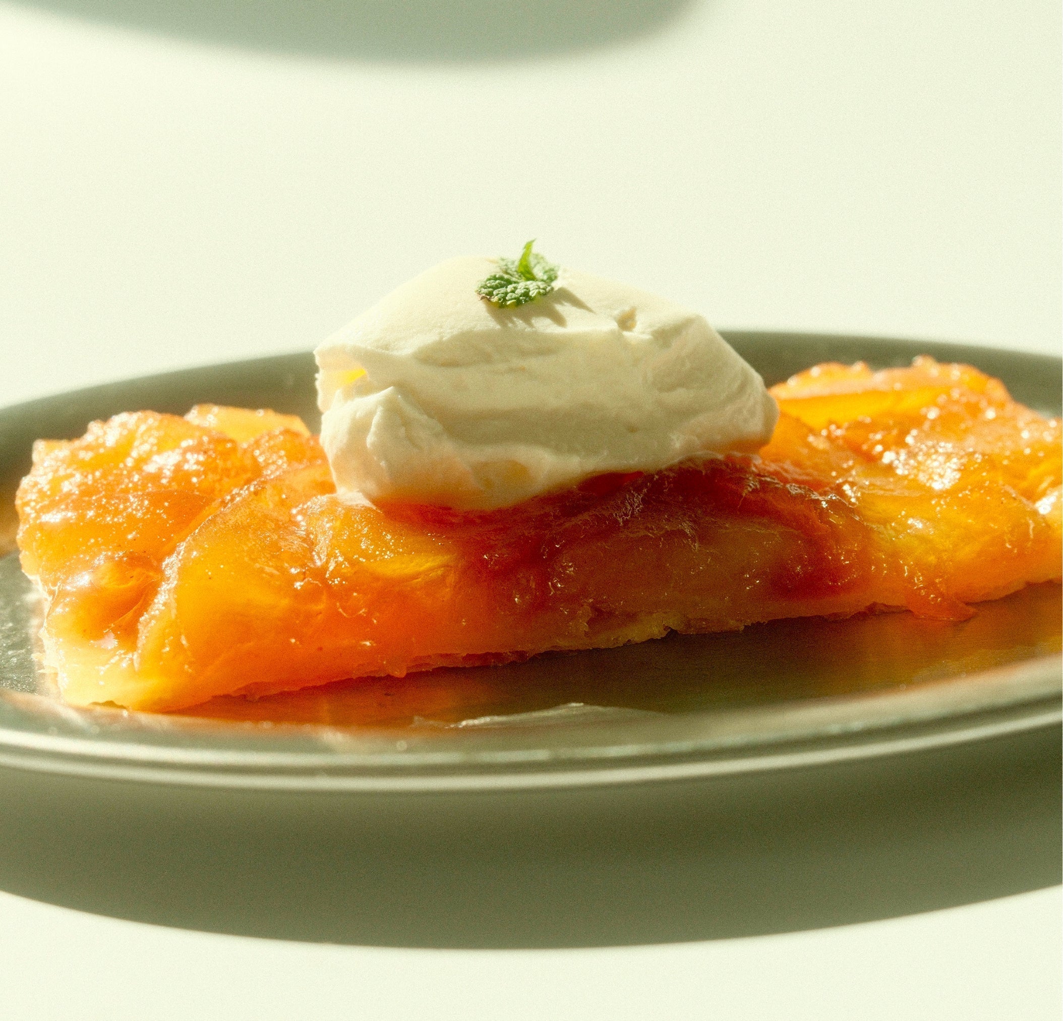 Close-up of yuzu apple tartine with caramelized apples and dollop of crème fraîche garnished with mint on white plate