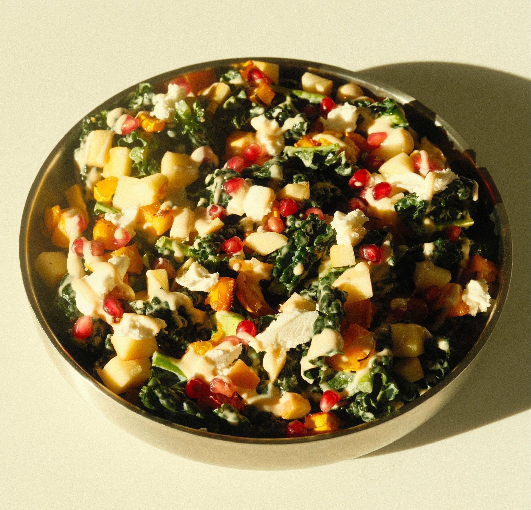 Overhead close-up of roasted squash and kale salad with pomegranate, squash, cheese, and yuzu tahini dressing