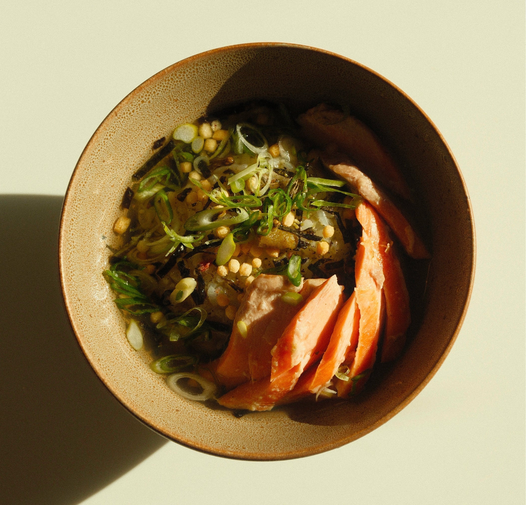 Top-down close-up of salmon ochazuke with sliced salmon, rice, scallions and crunchy rice pearls in a speckled bowl