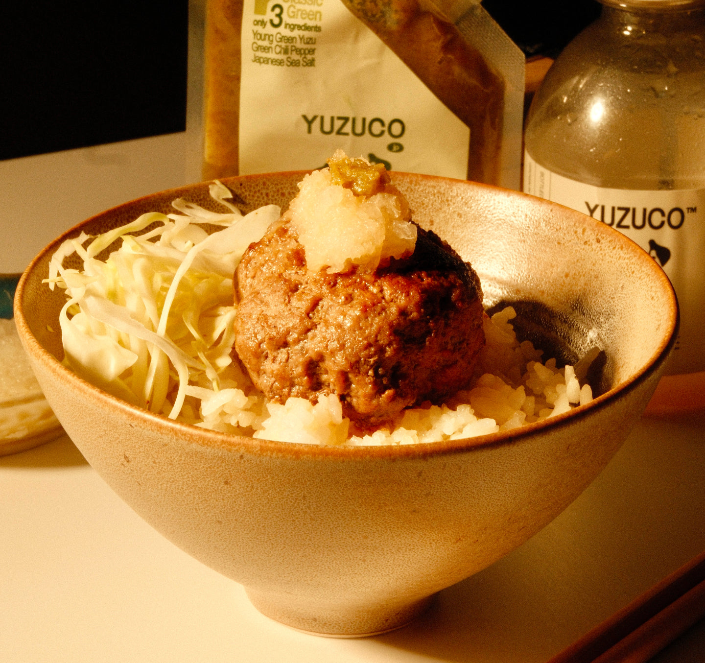 Hamburg patty on rice with shredded cabbage and grated daikon, YUZUCO bottle and sauce packet visible in background