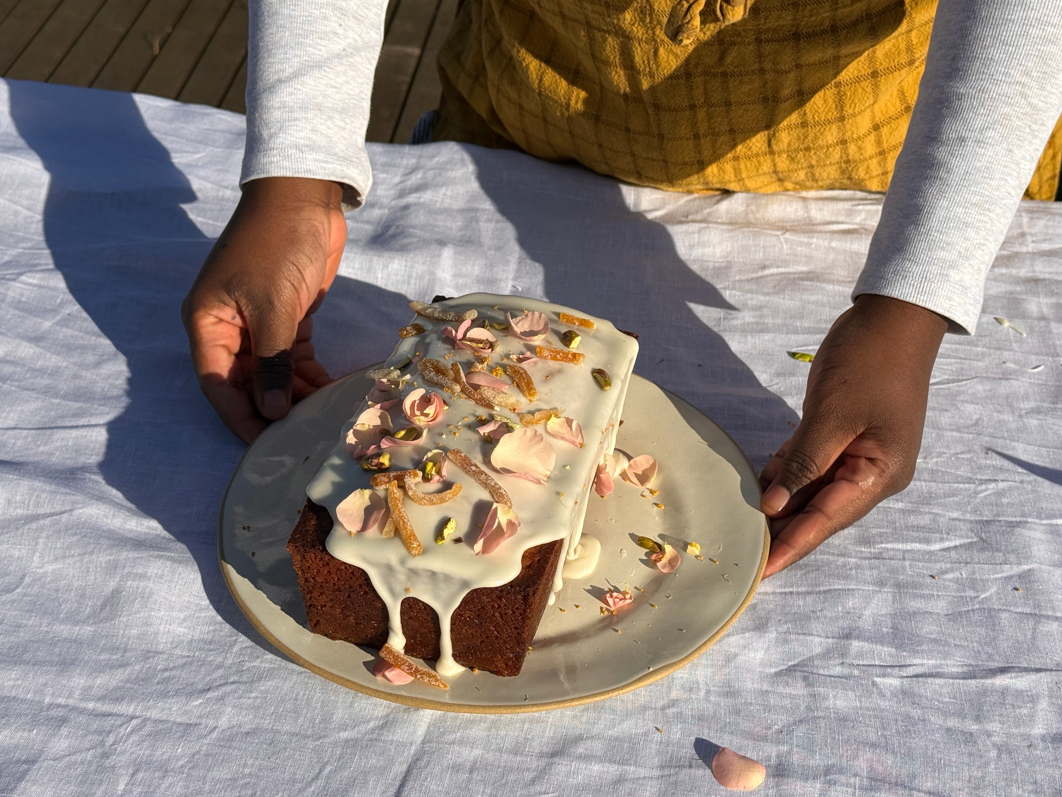 Hands placing a glazed yuzu kefir olive oil loaf on a ceramic plate atop a white linen tablecloth