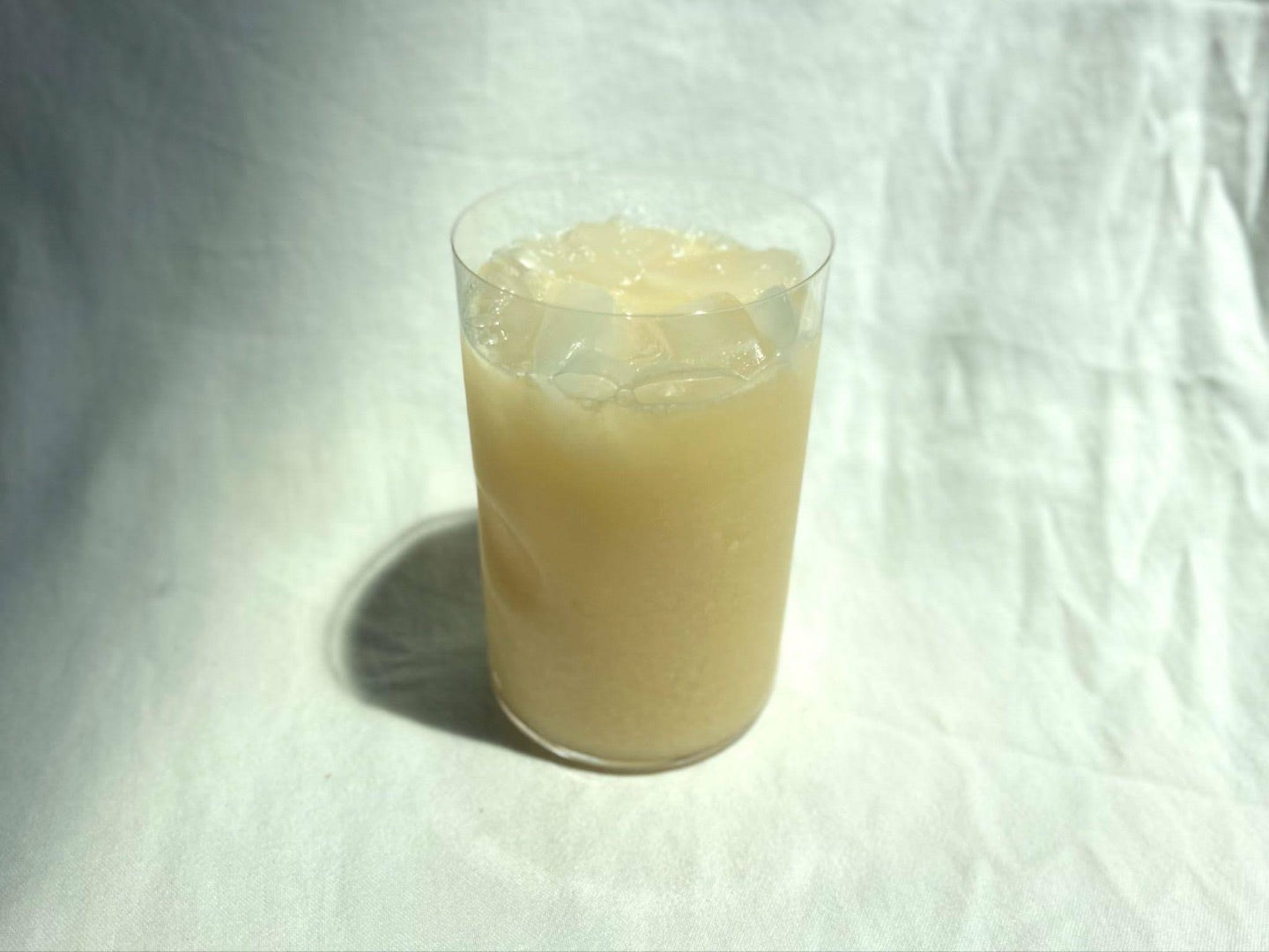 Slightly overhead view of a Creamy Tea Refresher in a clear glass with ice on a crumpled white cloth background