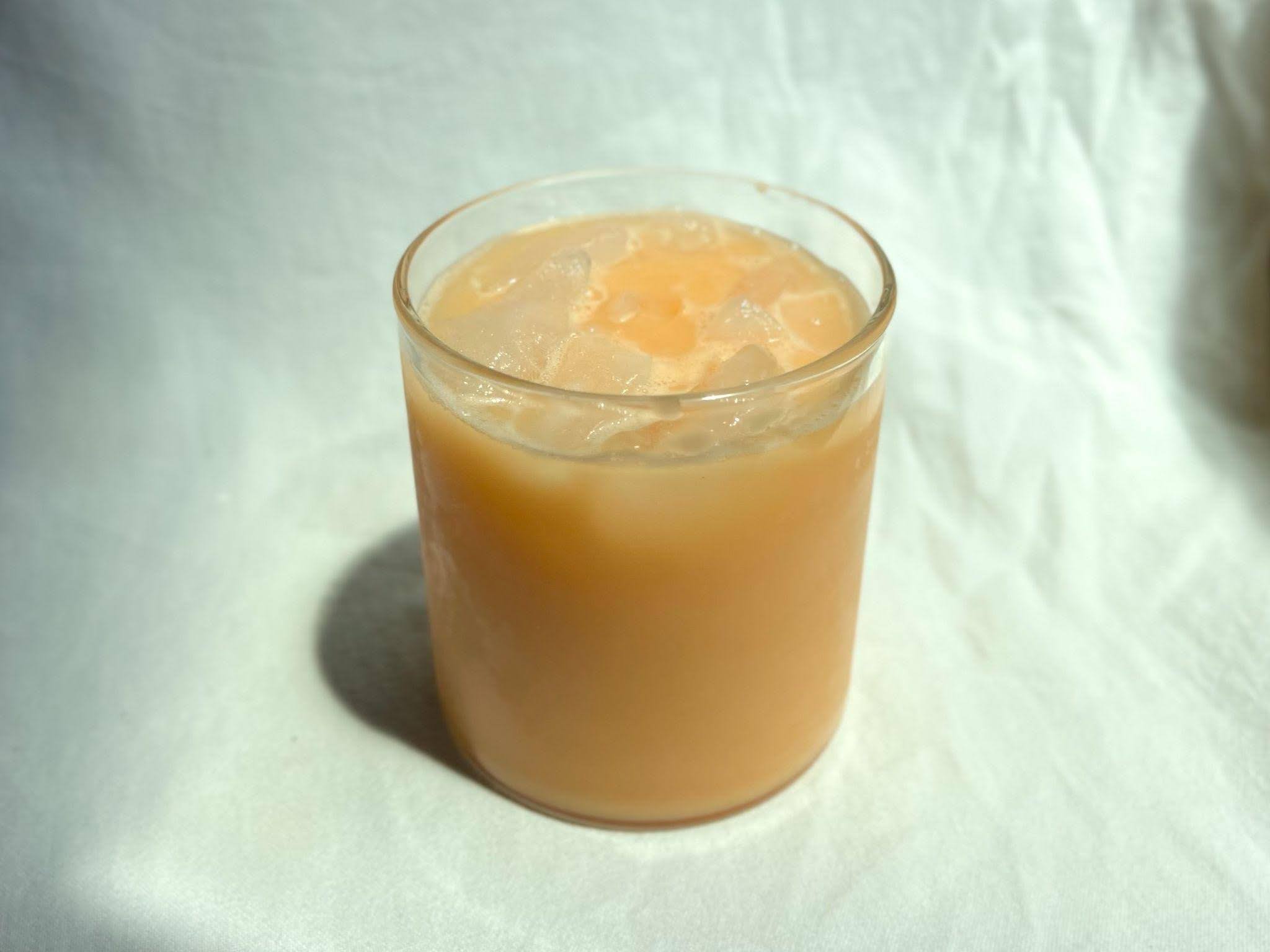 Cantaloupe cocktail in a short clear glass with ice, photographed on a white cloth backdrop