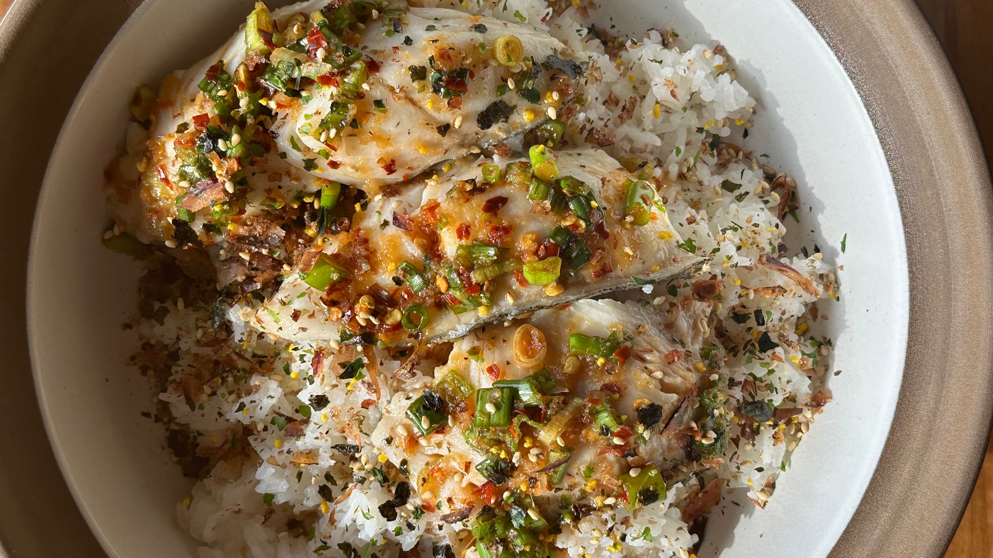 a bowl of vibrant yuzu cod over rice topped with delicious sauce and furikake. the bowl is a donabe and the recipe was created in collaboration between yuzuco and umamicart