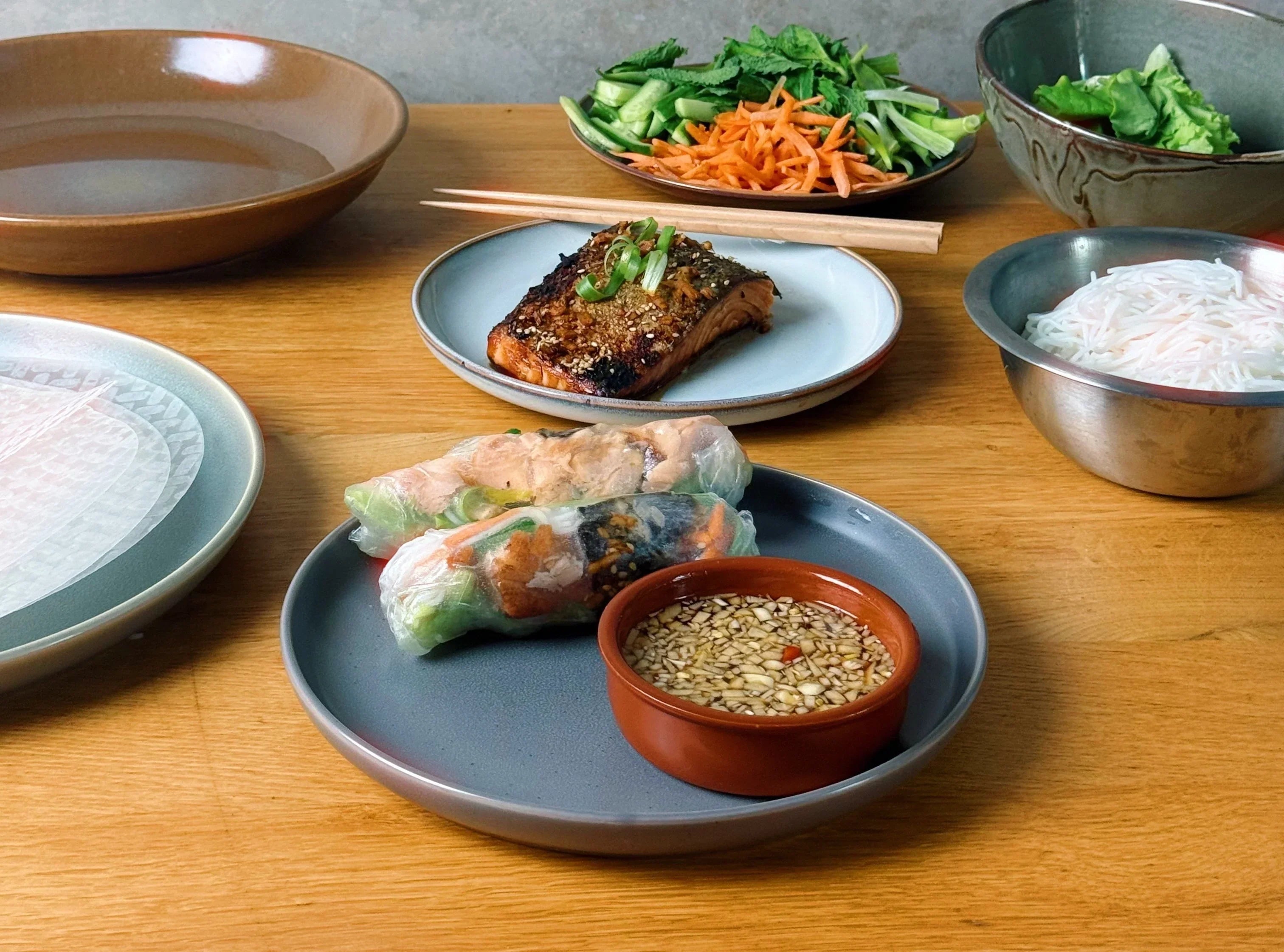 salmon yuzu spring rolls with fish sauce on a grey plate in the center
