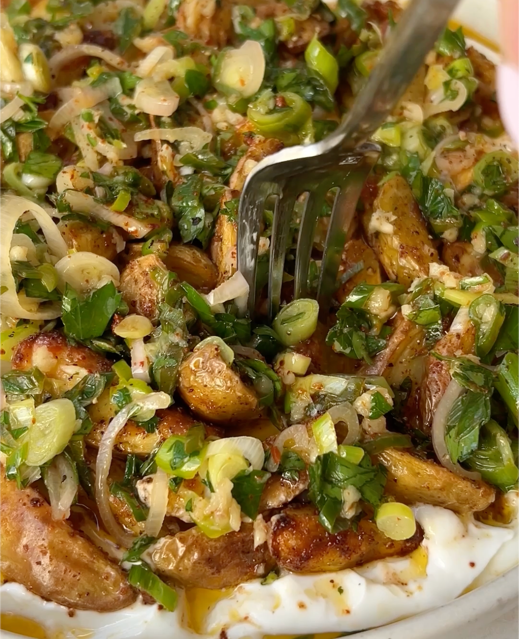 dish with potatoes on top of yogurt sauce topped with scallion, fork stabbing the middle 