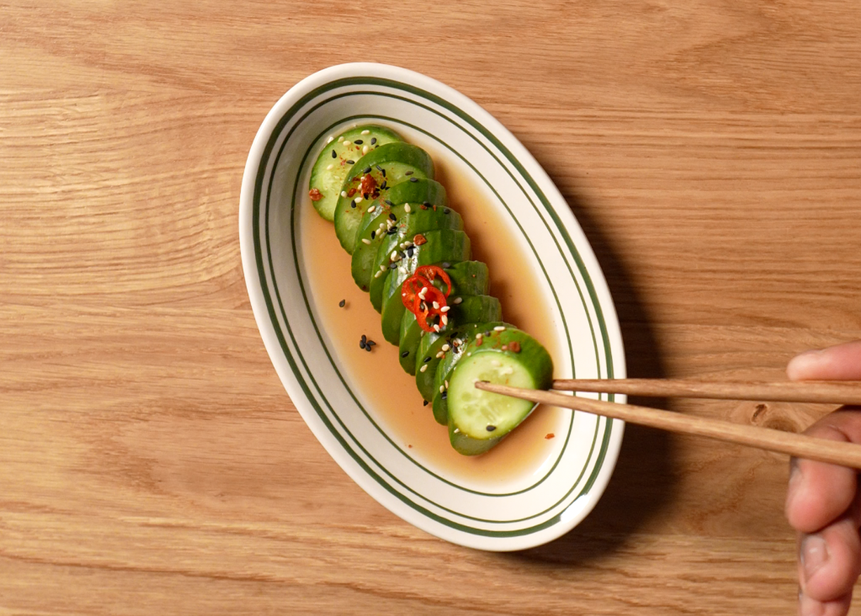 chopped up pickle lined up in a line with sliced red pepper and sesame seeds on top