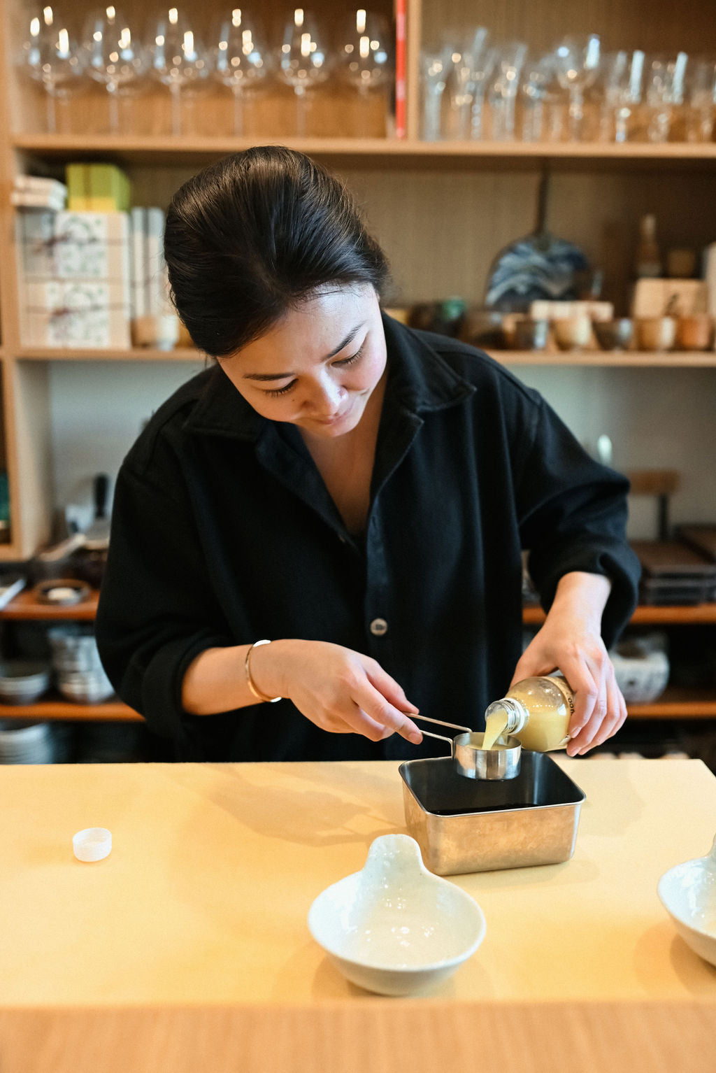 Chef Nan Yimcharoen pouring yuzuco 100% yuzu juice into ponzu container behind the wood bar at her restuarant KinKan in Los Angeles