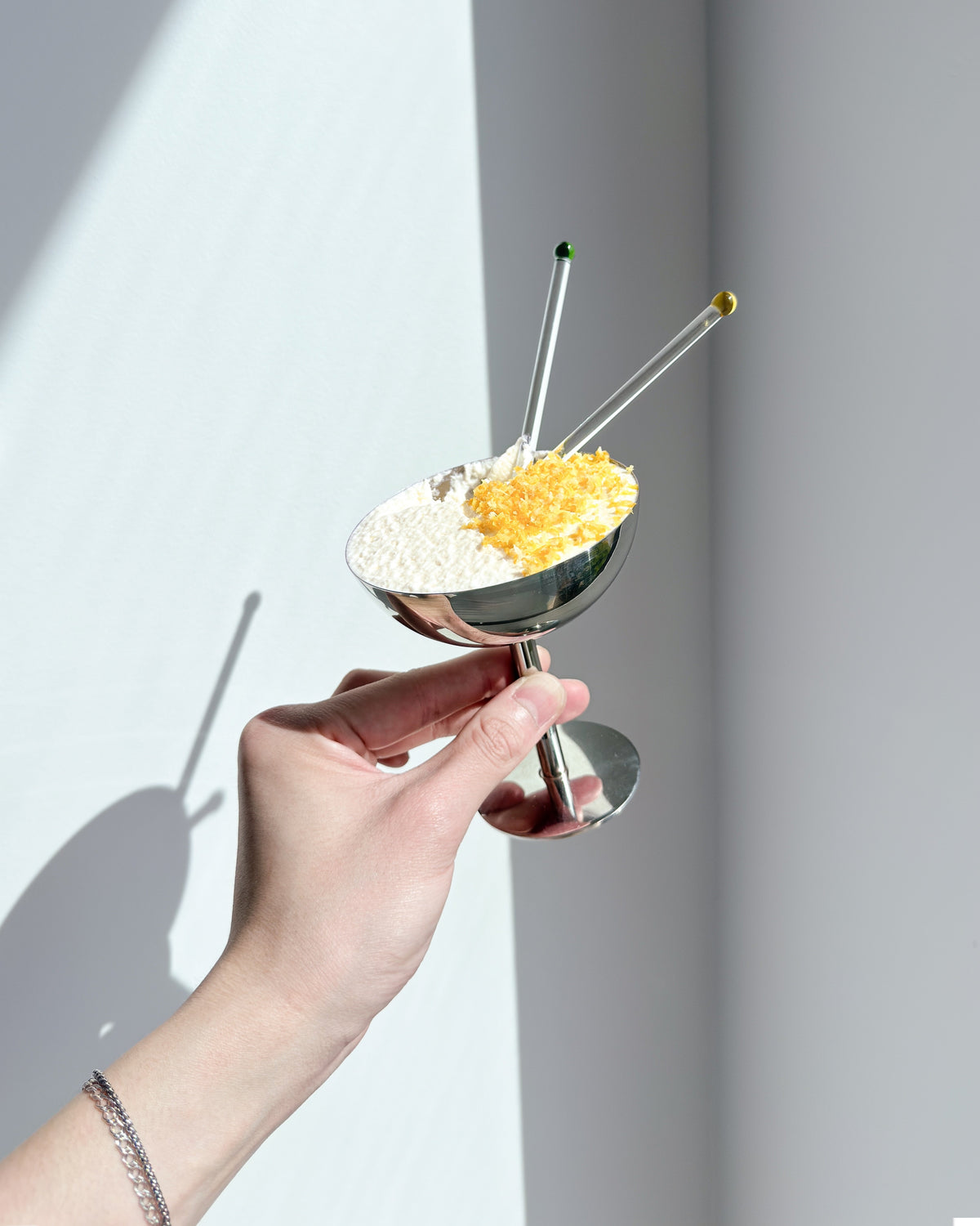 Hand holding a steel coupe filled with fluffy yuzu white chocolate mousse, topped with fresh citrus zest on one half