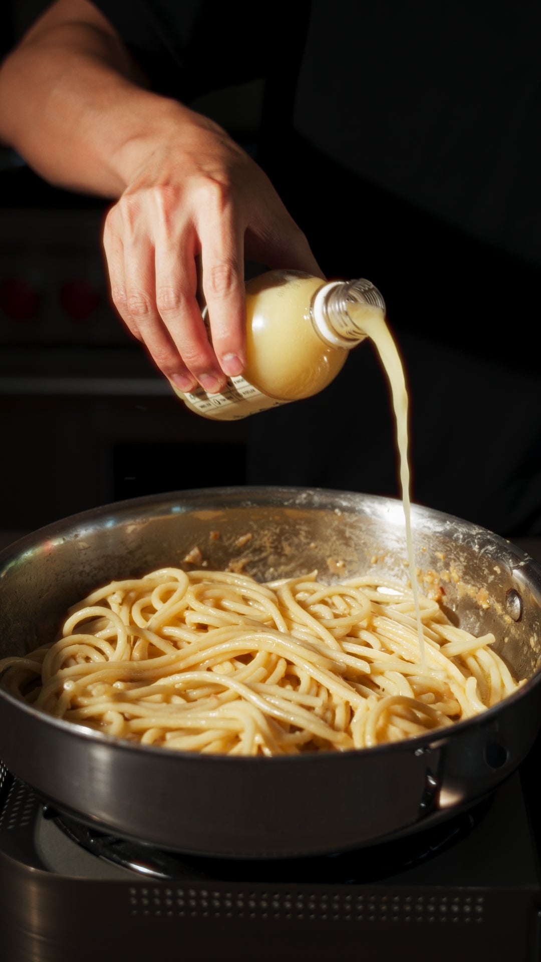 100% yuzu juice being poured into stainless steel pan with pasta front of a dark background
