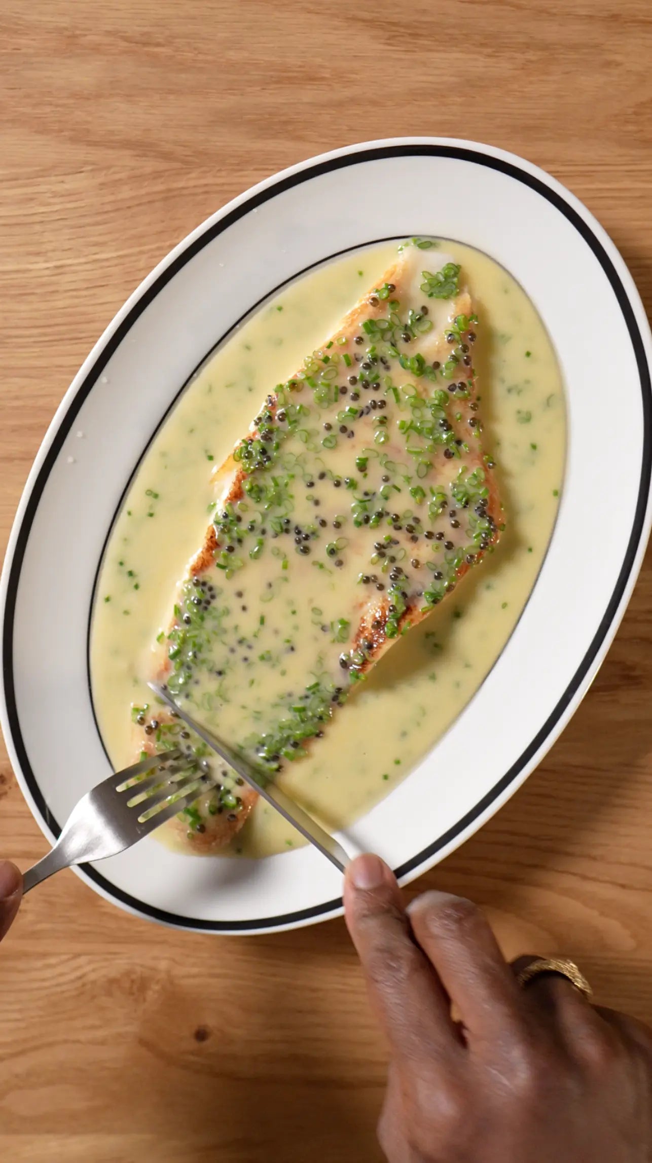 yuzu beurre blanc with shallot and sesame seeds over fish in a white dish