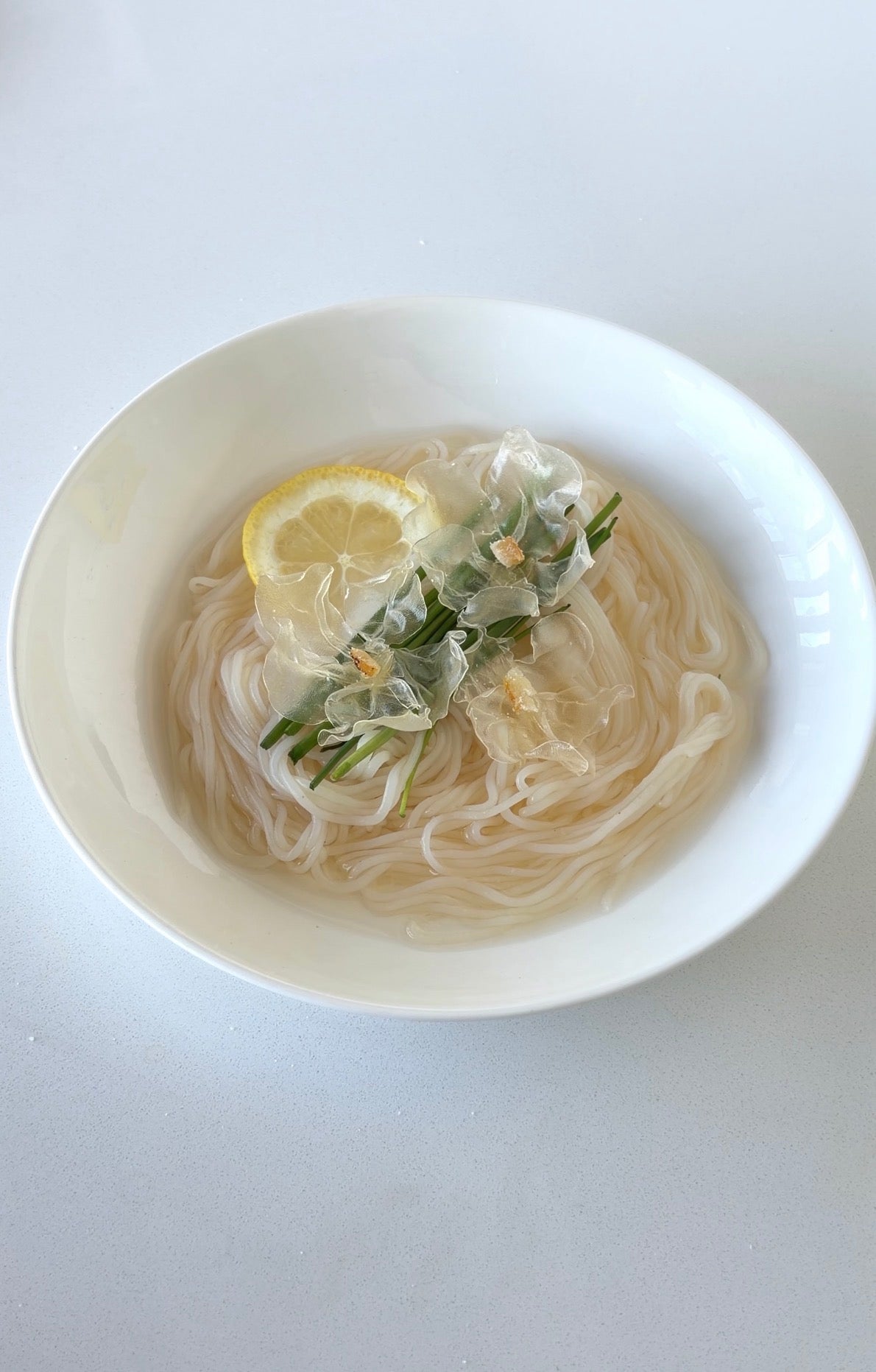 Yuzu Cold Noodles with crystal flowers topped with yuzu candy peel and a slice of lemon in a white bowl