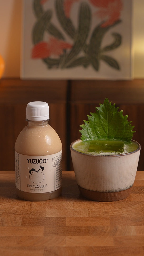A spicy shiso margarita served over ice in a ceramic cup, garnished with a shiso leaf and pictured beside a bottle of YUZUCO yuzu juice