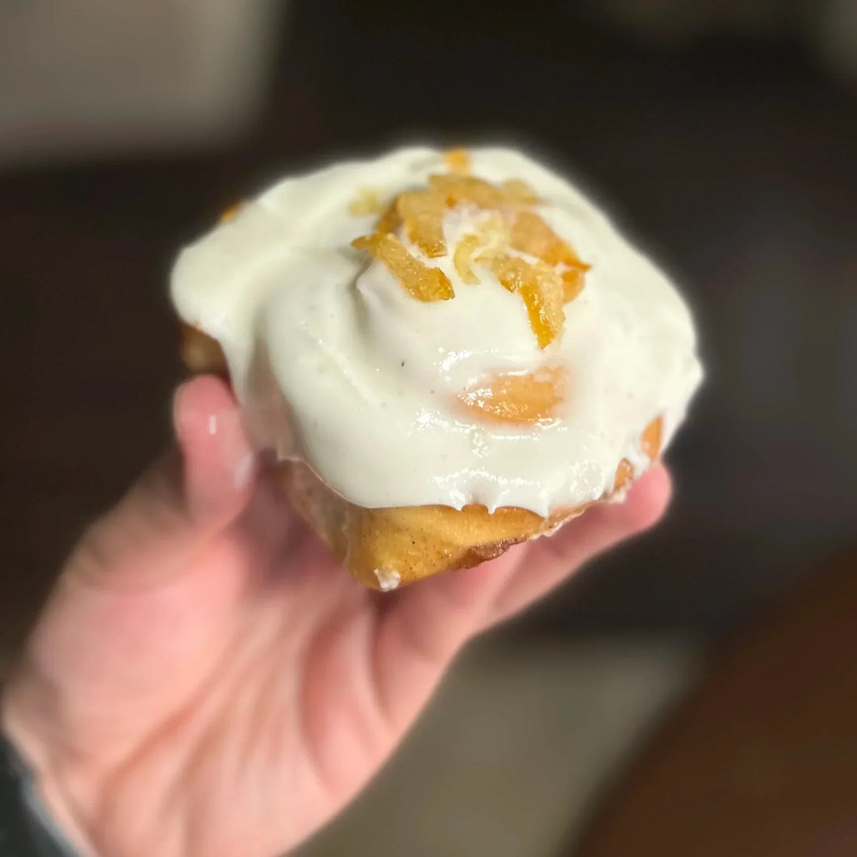 hand holding yuzu cinnamon roll with candied yuzu peel on top in the air