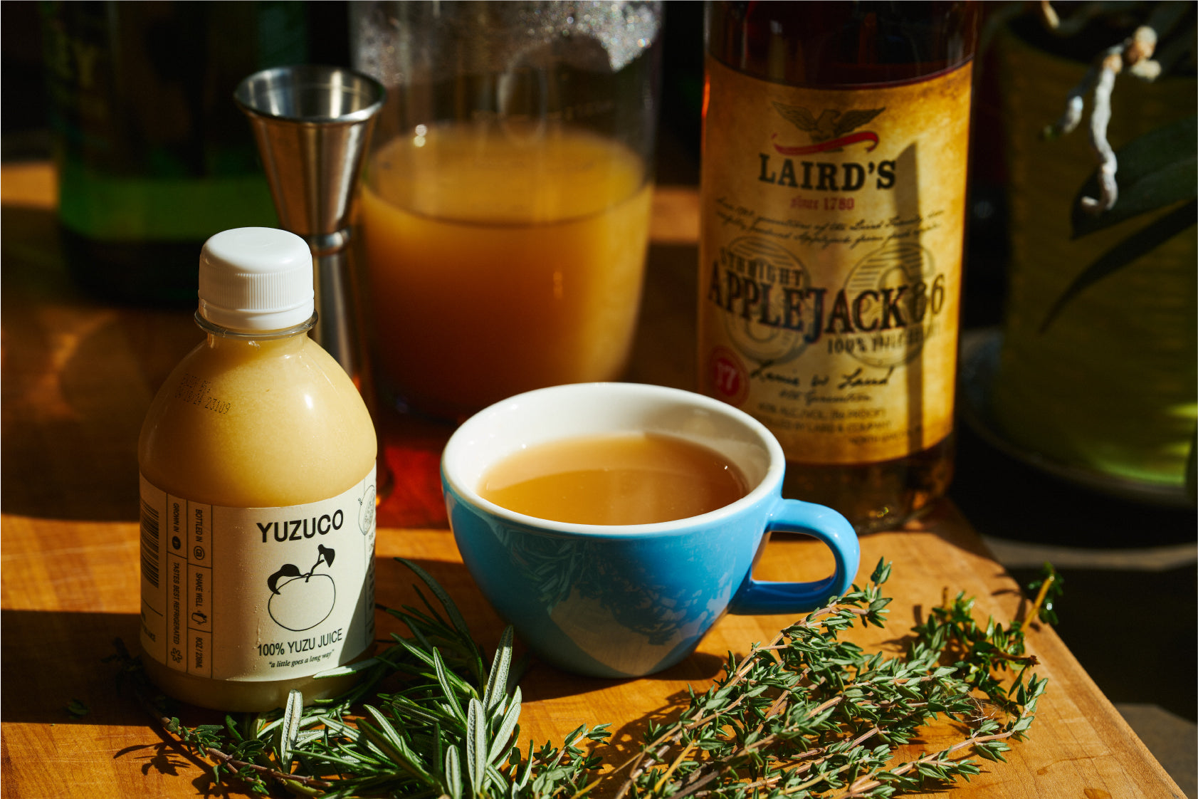 Yuzuco 100% yuzu juice with a mug of hot cider and fresh herbs