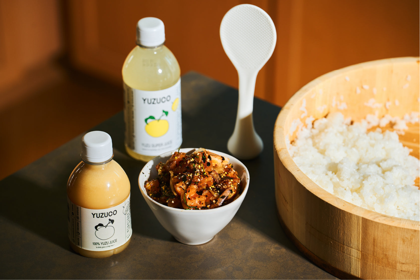 Yuzuco juice next to a wooden bowl of sushi rice and a smaller bowl with raw fish