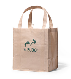 Front view of tan reusable grocery bag showcasing green YUZUCO logo, boxy gusseted sides, and top handles on white background