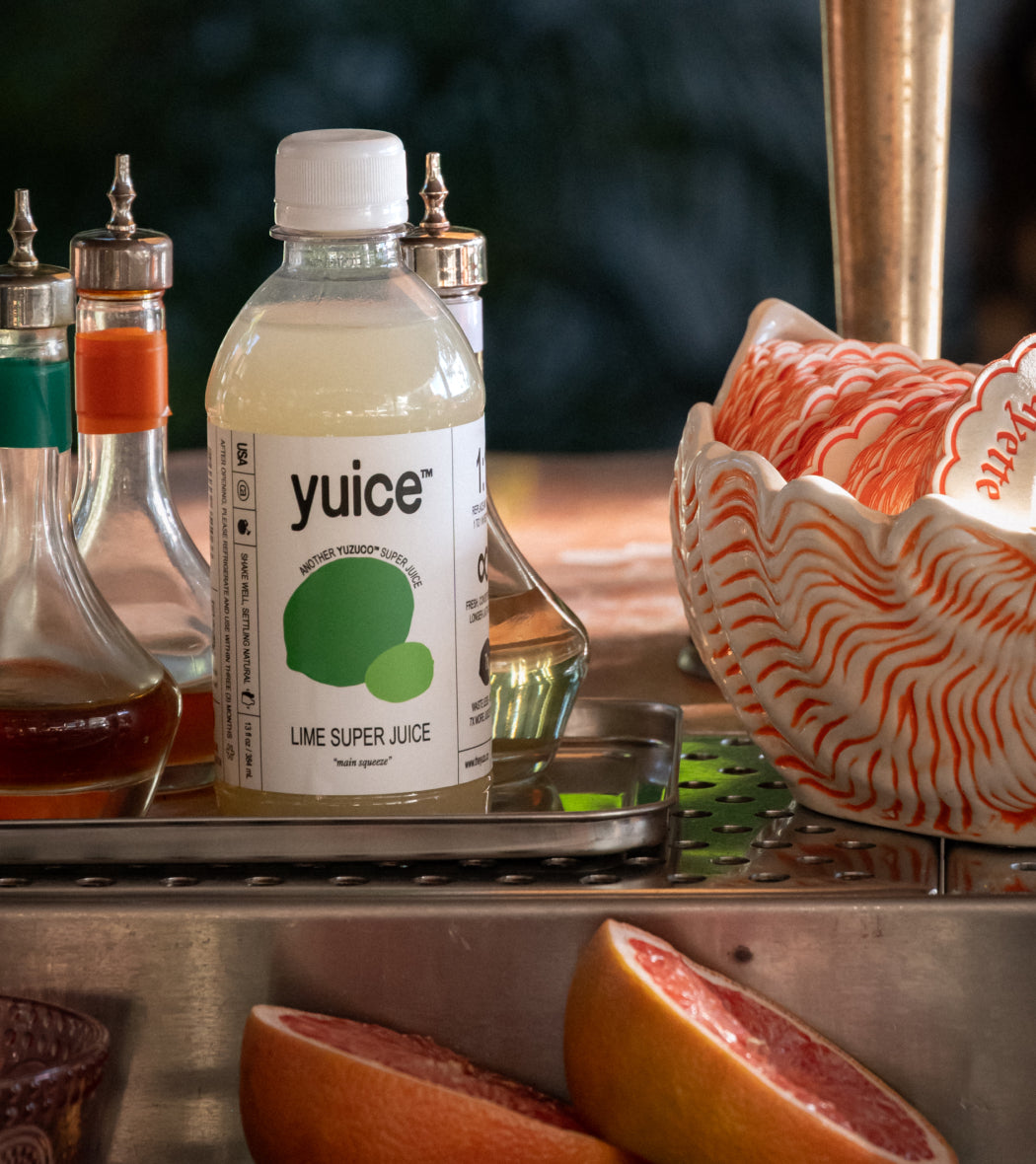 Front view of 13oz Lime Super Juice bottle showing yuice label and lime graphic on a metal tray with condiments