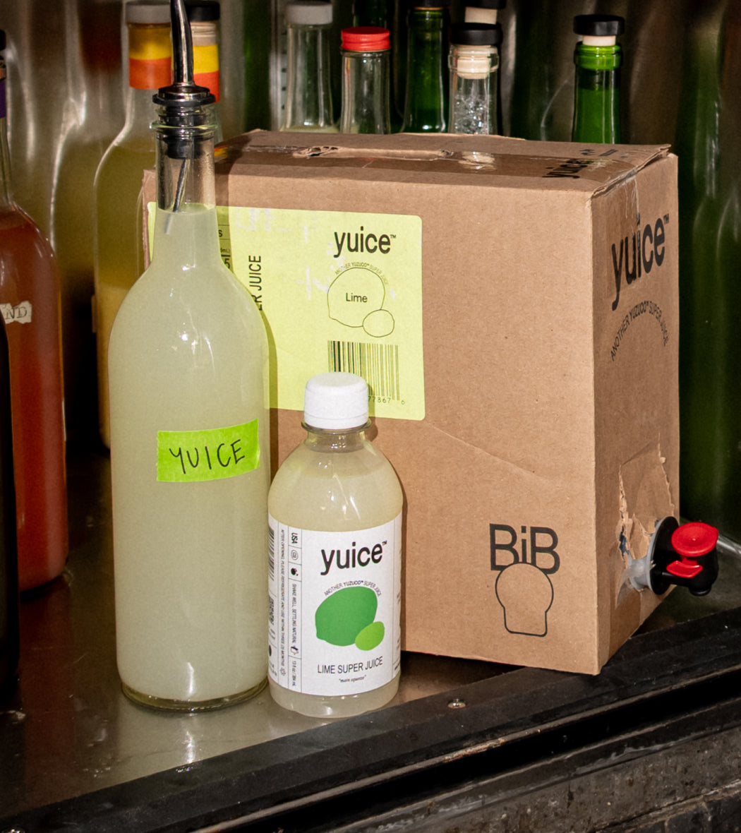 Front view of Lime Super Juice 13oz bottle and cardboard refill box with yuice label and tap on a metal counter