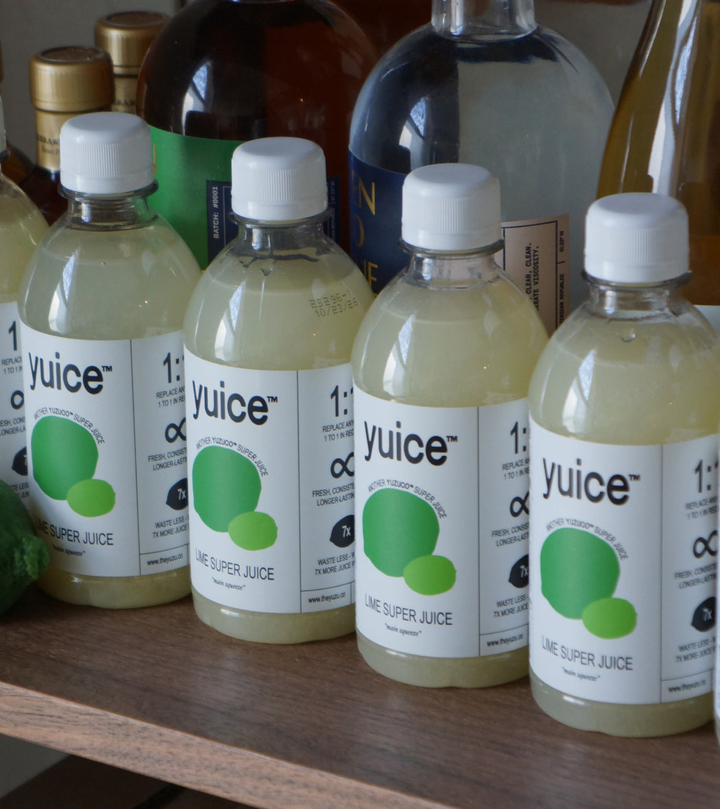 Front view of four 13oz Lime Super Juice bottles with white labels showing green lime graphics and yuice branding on a wooden shelf