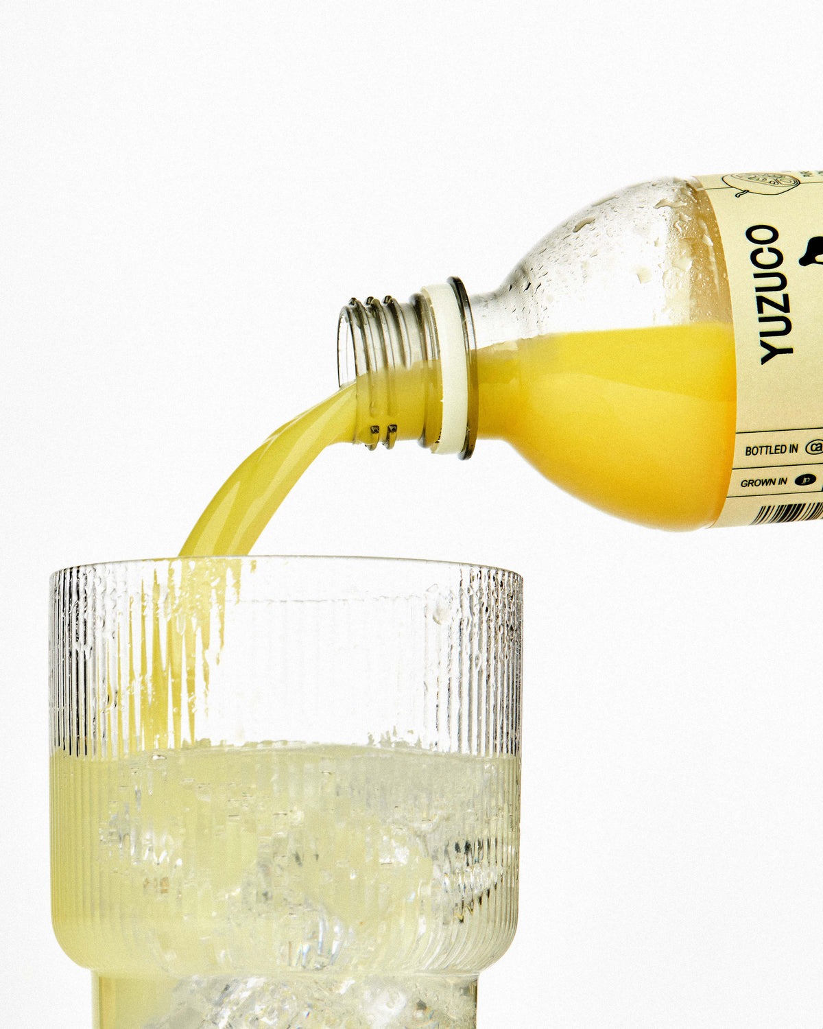 100% yuzu juice pouring into a glass with sparkling water and ice