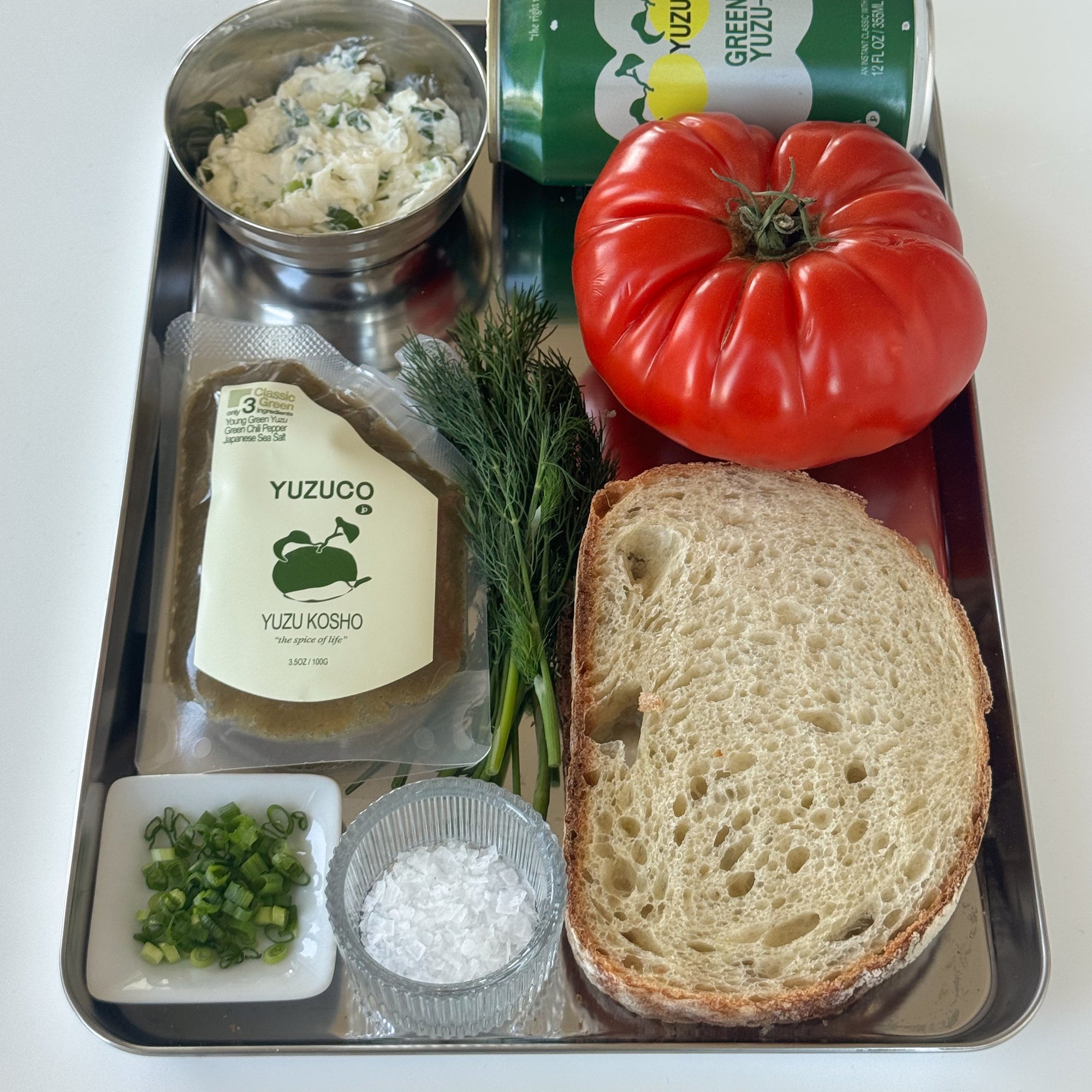 Tray with bread, tomato, yuzu kosho, and other ingredients on a white background