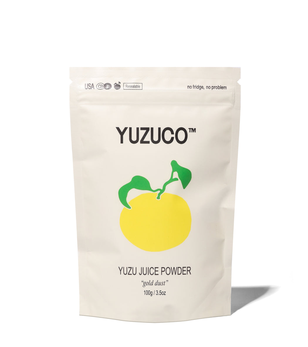 Front view of YUZUCO Yuzu Juice Powder pouch showing yellow yuzu illustration, gold dust label and 100g (3.5 oz) weight on white background
